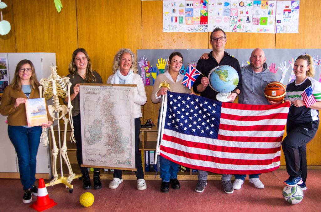 Die Lehrerinnen und Lehre des bilingualen Unterrichts halten eine USA Flagge und Karte in der Hand