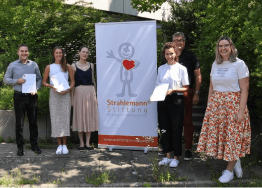Sechs Personen stehen im Freien vor einem Banner der Strahlemann Stiftung
