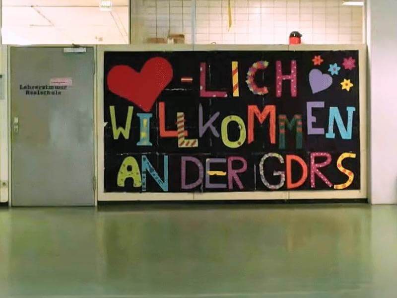 Foto vor dem Lehrerzimmer der Schule. Daneben ist ein großes Plakat auf dem "Herrlich Willkommen an der GDRS" steht